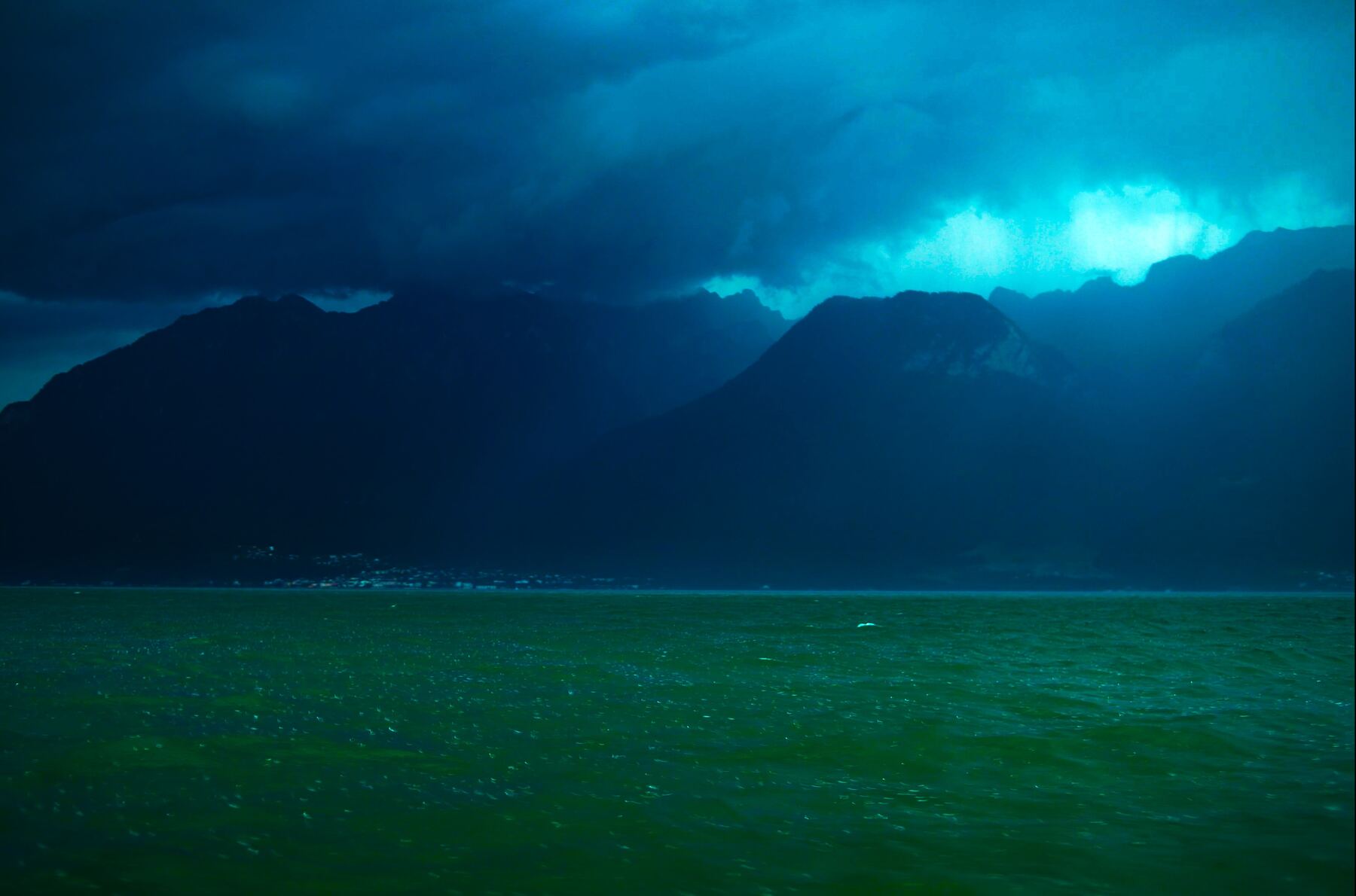 A tempestade sobre o lago, a água verde sob montanhas azul-negras